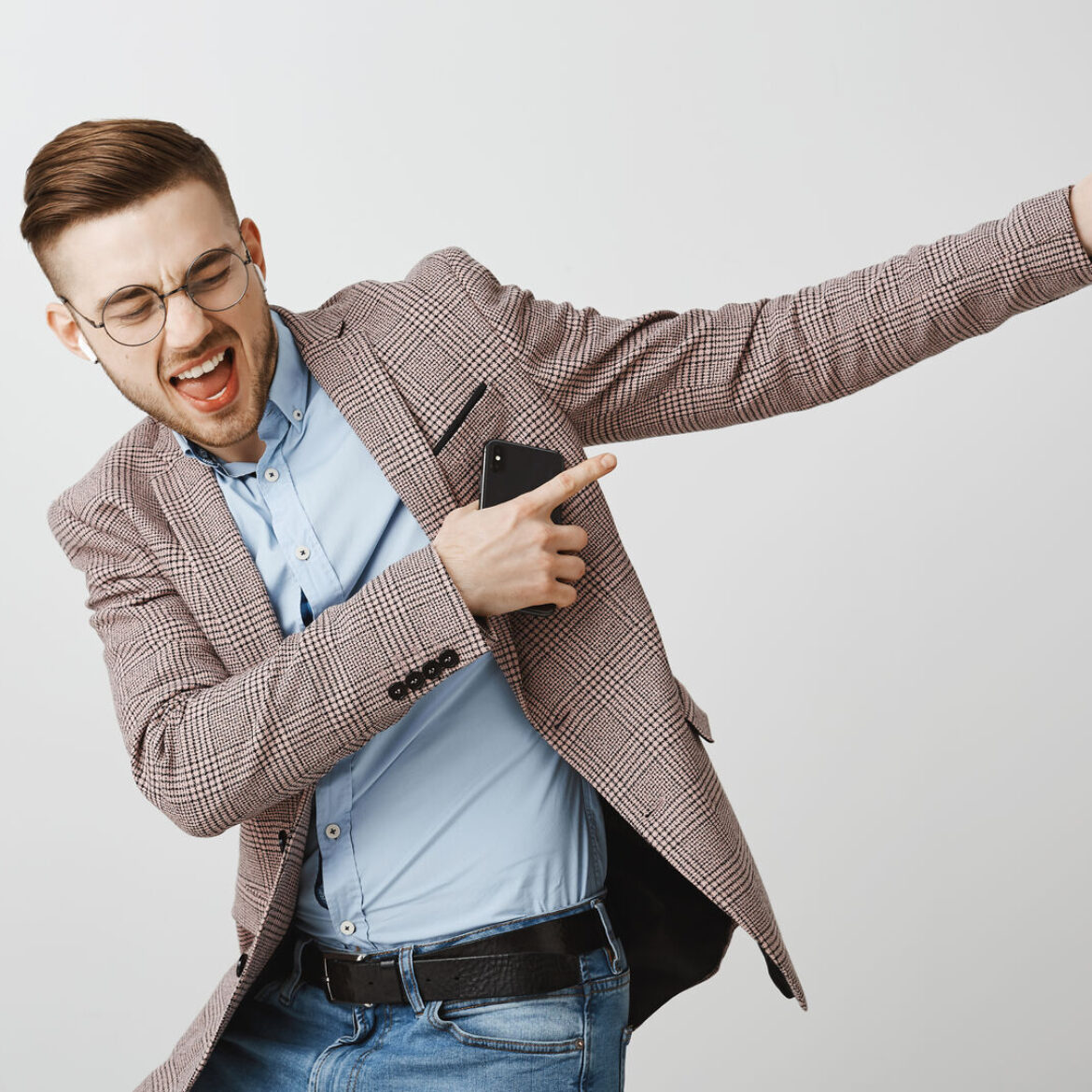 Boosting mood and confidence with right track. Delighted good-looking joyful man with bristle in trendy jacket singing dancing pointing at upper right corner listening music in wireless earbuds