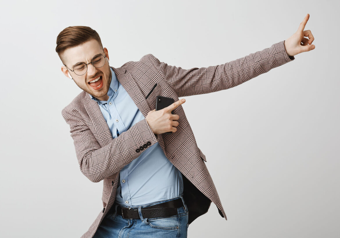 Boosting mood and confidence with right track. Delighted good-looking joyful man with bristle in trendy jacket singing dancing pointing at upper right corner listening music in wireless earbuds