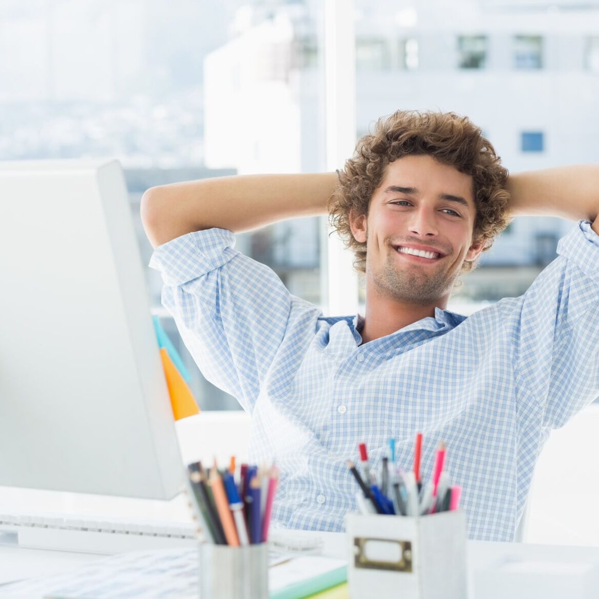 Relaxed smiling casual young business man with computer in a bright office